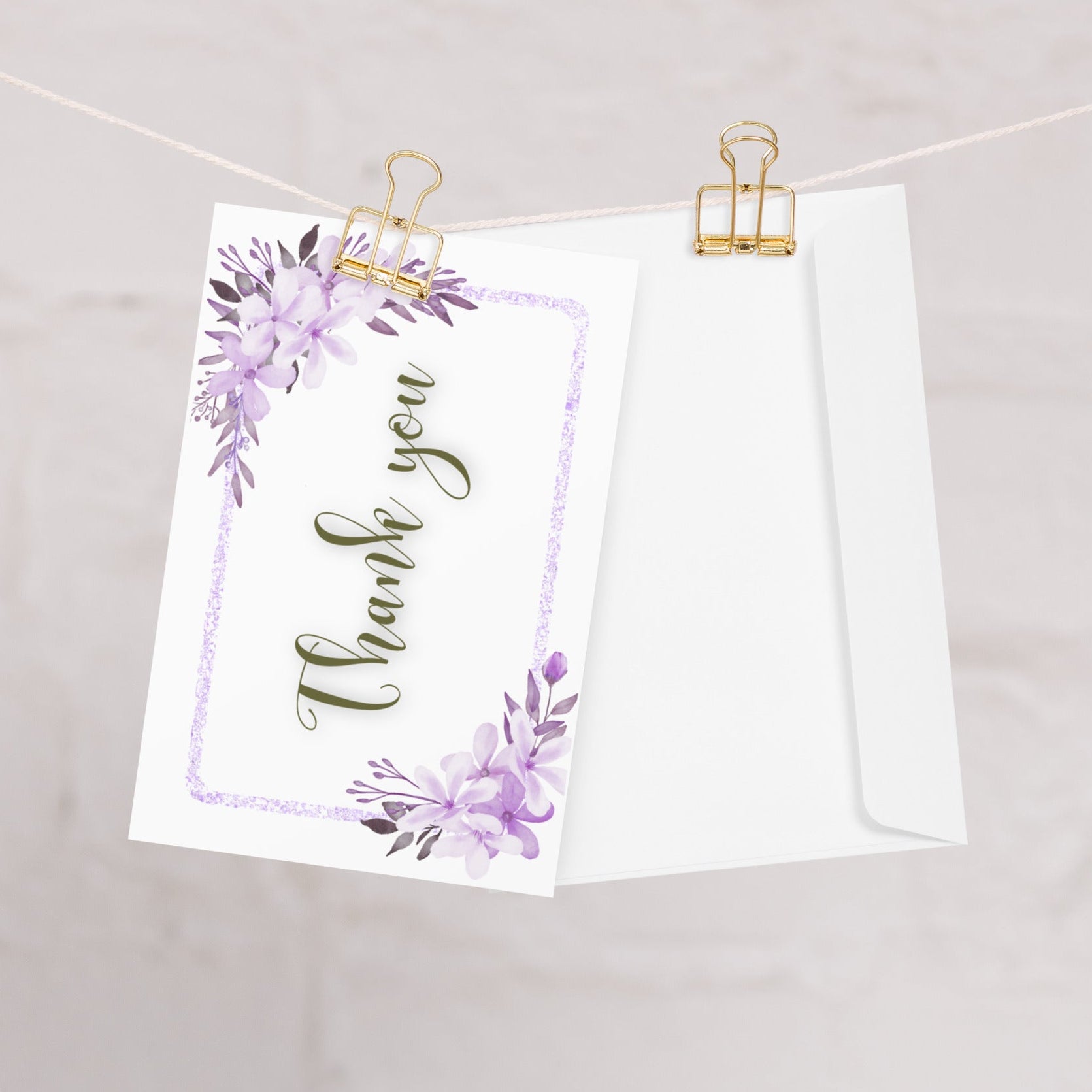 Greeting card with 'Thank you' text and floral design hanging on a string with gold clips.