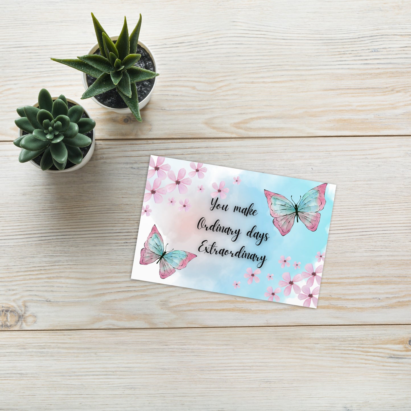 Motivational card with butterflies and text on a wooden surface with small plants.