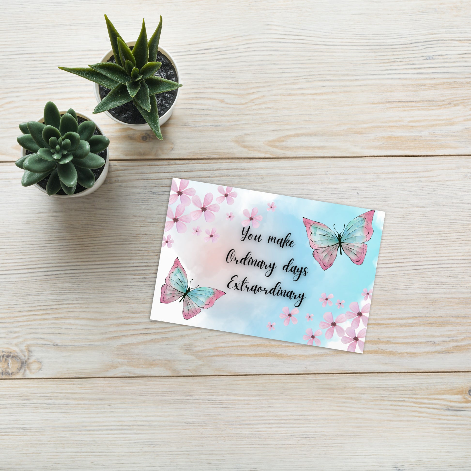 Motivational card with butterflies and text on a wooden surface with small plants.
