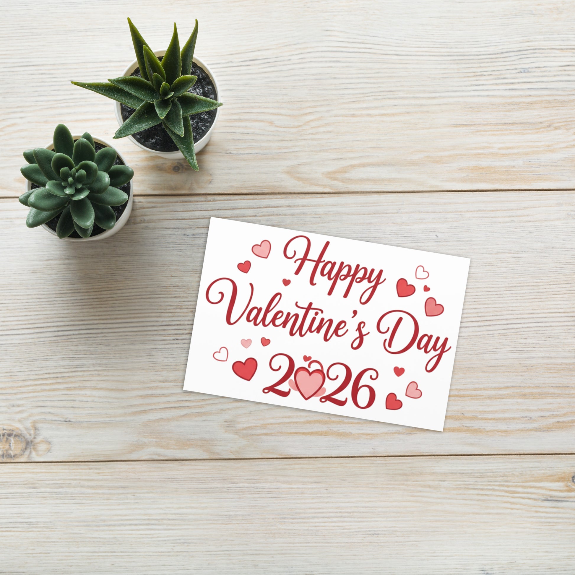 Valentine's Day card with 'Happy Valentine's Day 2026' on a wooden surface with small potted plants.