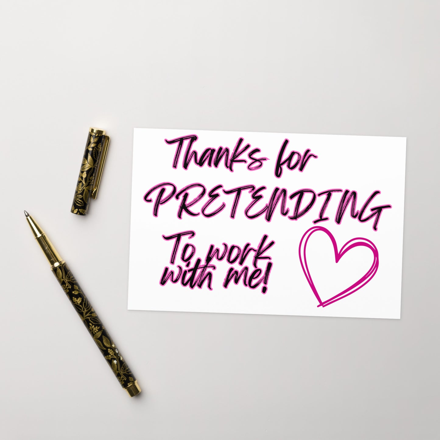 Note with 'Thanks for pretending to work with me!' text and a heart symbol, accompanied by two pens on a light gray background.
